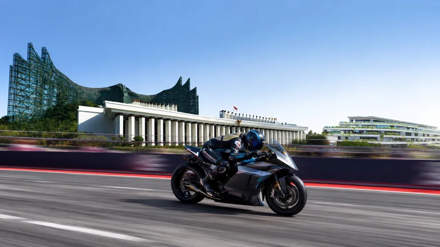 An electric race bike at speed on the Sumbu Timur circuit, with Istana Garuda behind it.